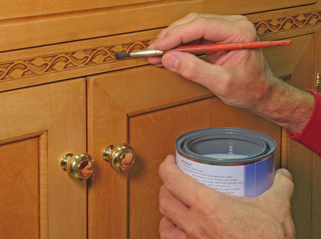 Closeup of painter apply vanish to the inlaid trim of a handcrafted cabinet