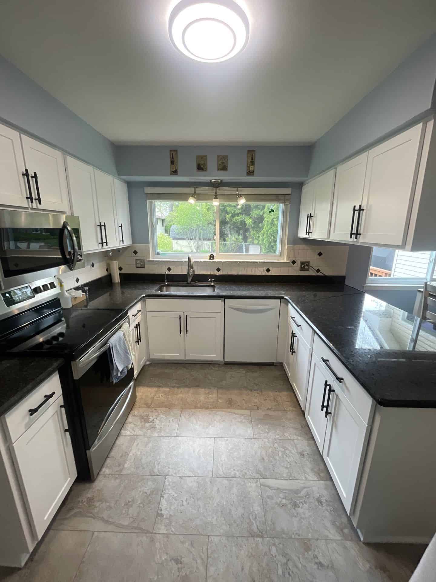 A freshly painted U shaped kitchen featuring white cabinets, black countertops, and a light blue accent wall.