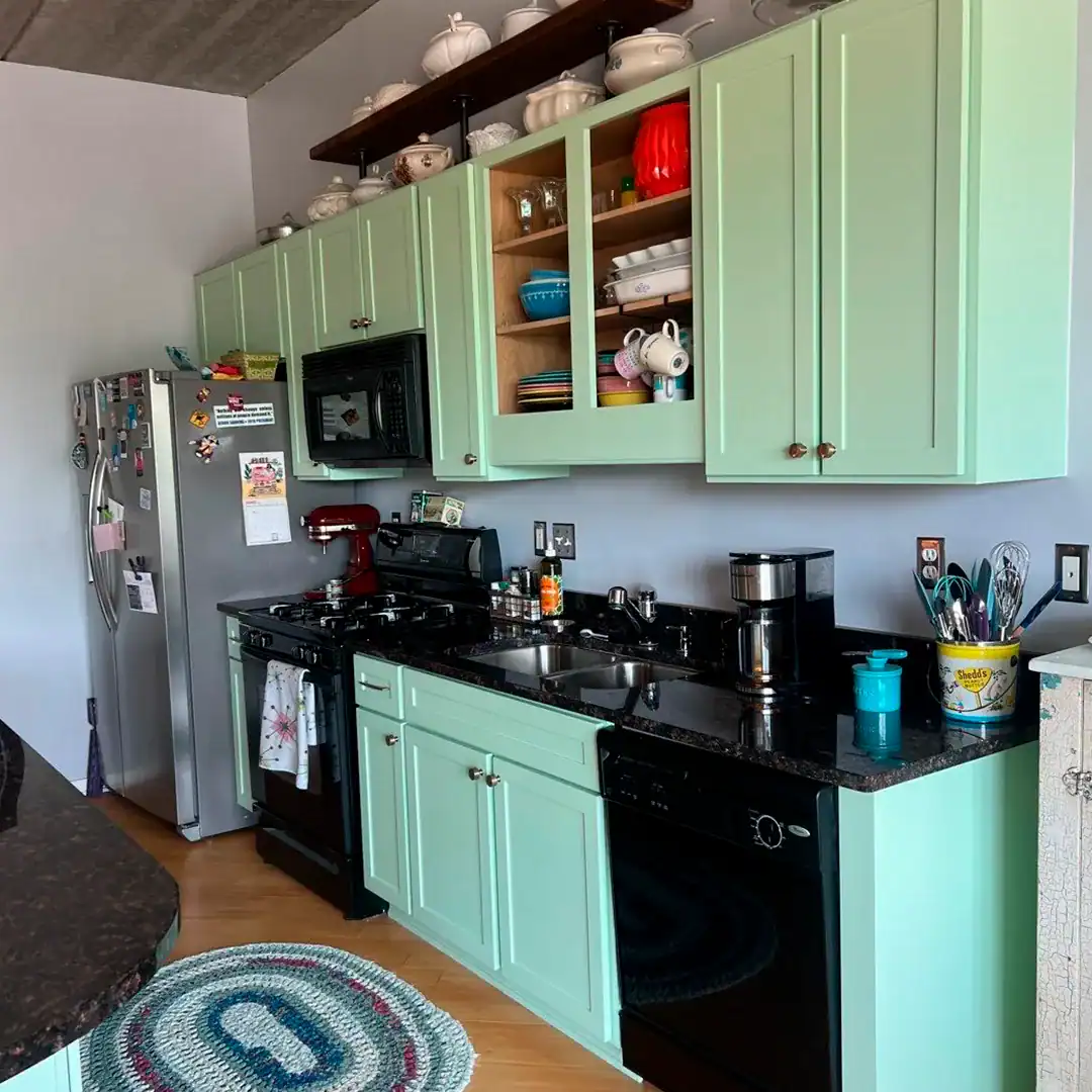 Mint green painted kitchen cabinets with black granite countertop and black appliances in Warren home