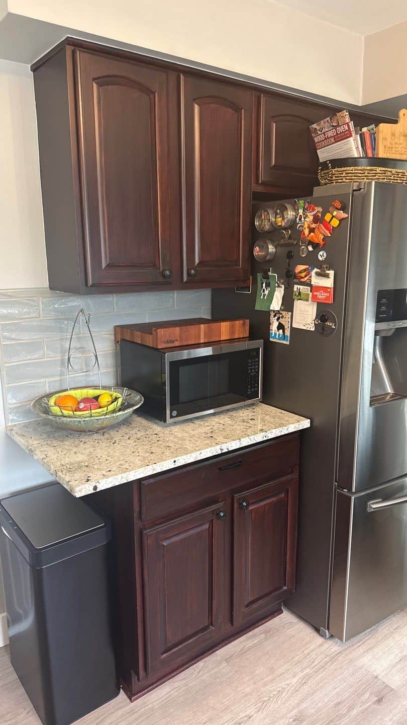 Dark Cherry Kitchen Cabinets Before Dark cherry-stained kitchen cabinets with arched recessed panel doors, speckled granite countertop, and black microwave